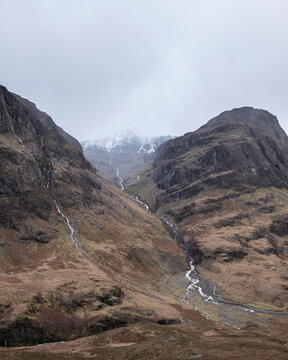 Majestic moody landscape image of Three Sisters in Glencoe in Scottish Highlands on a wet Winter day wit high water running down mountains