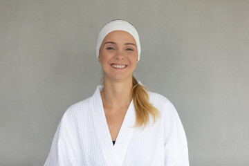 Cute teen caucasian woman with white towel folding around head in white spa dress smile and pose to camera.