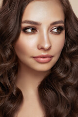 Fototapeta premium Brunette girl with perfect makeup. Smiling beautiful model woman with long curly hairstyle. Care and beauty hair products.