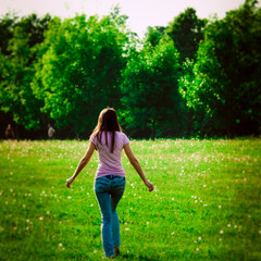 Back view of girl walking at green field. Outdoor summer portrait of teen girl on green meadow.