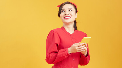 Portrait of a smiling young casual asian woman looking at mobile phone isolated over yellow background
