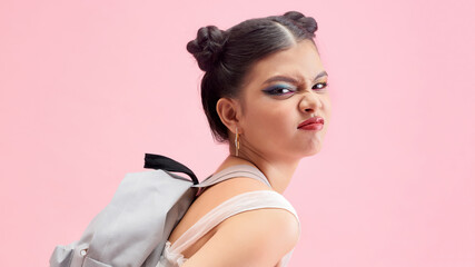 Full length portrait of a smiling woman with backpack standing on pink background and looking at camera