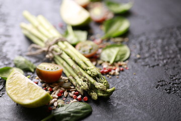 Fresh green vegetables, tomatoes, spinach, lime. Raw asparagus with spices on a black table. Background image, copy space, horizontal, rustic