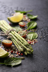 Fresh green vegetables, tomatoes, spinach, lime. Raw asparagus with spices on a black table. Background image, copy space, vertical, rustic