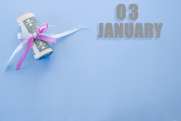 calendar date on blue background with rolled up dollar bills pinned by blue and pink ribbon with copy space. January 3 is the third day of the month