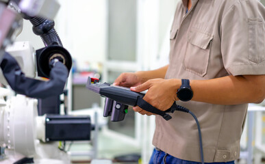 Smart factort concept: An engineer use handheld controller setting industrial robot in production plant.