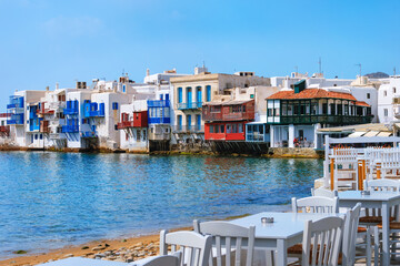Fototapeta na wymiar Beautiful Little Venice, Mykonos, Greece. Romantic neighborhood with whitewashed bars, cafes, restaurants. Colorful tables and chairs by shoreline