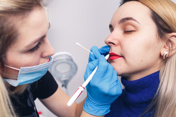 The beautician prepares the lips for permanent makeup, the model looks in the mirror.