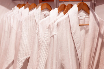 White bathrobes hang on wooden hangers.