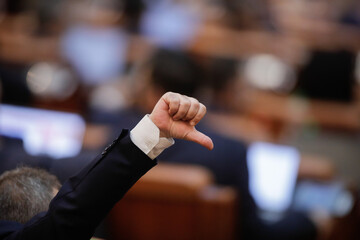 Fototapeta na wymiar Romanian members of parliament gesture to their colleagues how to vote bills in a plenary sitting with both chambers reunited (Chamber of Deputies and Senate), in the Palace of Parliament.