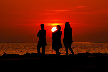 People strolling by the sea at sunset. Silhouettes.