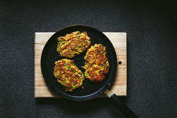 Vegetable zucchini and carrot fritters on a frying pan and a wooden cutting board, top view photo with copy space