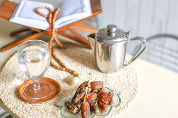 Top view of kurma or dates fruit with glass of water, holy book Al-Quran, teapot and prayer beads on the table. Traditional Ramadan, iftar meal. Ramadan kareem fasting month concept