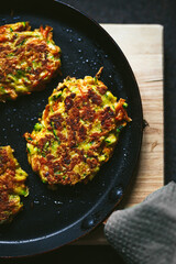 Vegetable zucchini and carrot fritters on a frying pan and a wooden cutting board, close-up top view photo
