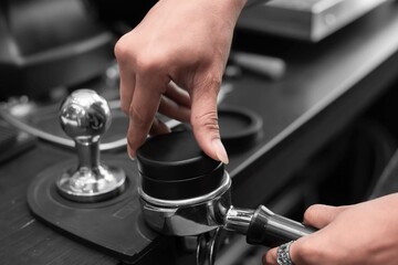 Closed up of barista’s hand tamping the portafilter before making fresh coffee in a coffee shop. 