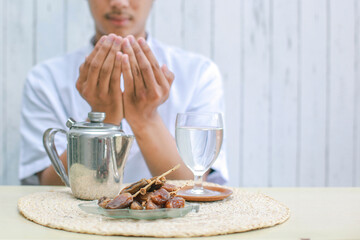 Iftar dish with muslim man hand praying to Allah. Dates fruit with glass of mineral water and teapot on the table. Traditional Ramadan, iftar meal. Ramadan kareem fasting month concept. - obrazy, fototapety, plakaty