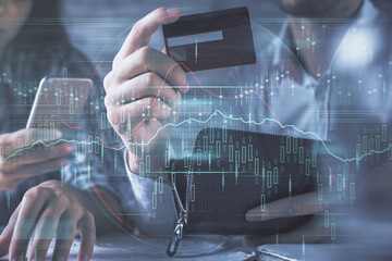 Double exposure of man and woman on-line shopping holding a credit card and forex graph hologram drawing. Stock market E-commerce pay on-line concept.