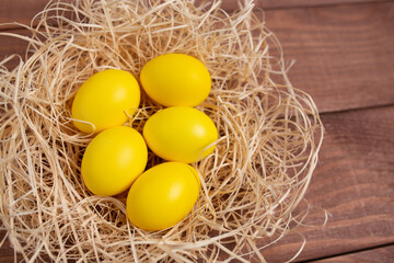 Fototapeta na wymiar Nest with yellow eggs on a wooden background. Happy Easter. Trendy colour 2021. 