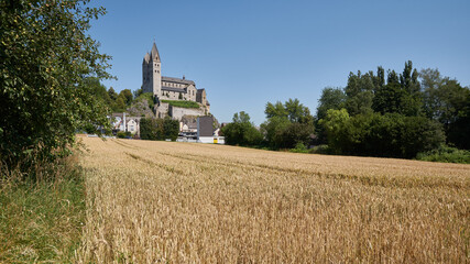 Fototapeta na wymiar Blick über ein goldenes Getreidefeld auf die St. Lubentius Basilika in Dietkirchen