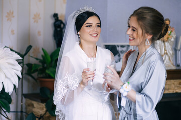 A beautiful and elegant bride with bridesmaids, dressed in an elegant robe, holding a glass of champagne, smiling.