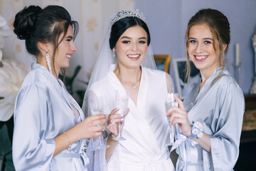 Gorgeous bride and bridesmaids drink champagne and have fun on wedding morning. Cheerful young...