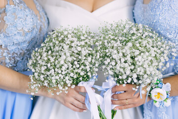The bridesmaids and the bride hold modern wedding bouquets of white flowers and greenery with...