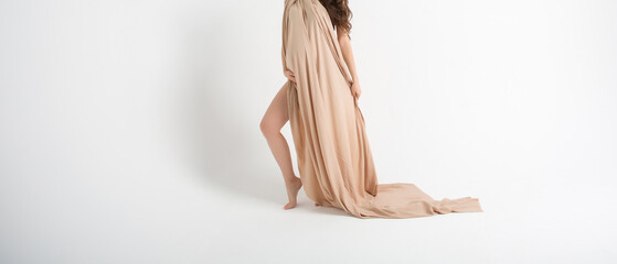 Pregnant woman in long light fabric around her body, arms wrapped around baby in her belly on white background