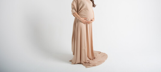 Pregnant woman in long light fabric around her body, arms wrapped around baby in her belly on white background