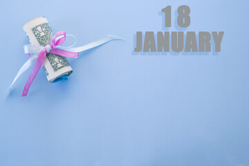 calendar date on blue background with rolled up dollar bills pinned by blue and pink ribbon with copy space. January 18 is the eighteenth day of the month
