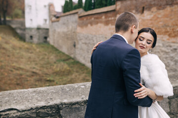 Fototapeta na wymiar Fashionable and stylish portrait of beautiful newlyweds on a walk by a brick wall.