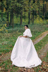 Portrait of a beautiful bride in a wedding dress with a long train walking along the road in the park, back view.