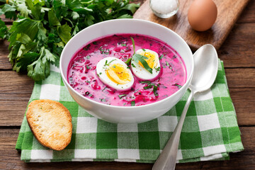 Traditional cold summer beetroot soup with vegetables and boiled egg in a white bowl on wooden...