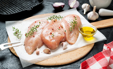 Raw chicken fillet with garlic, pepper and fresh thyme on black stone background. 