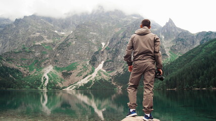 A man climbs a stone near the shore of a picturesque mountain lake with emerald water. Great views of nature. Travel and healthy lifestyle concept.