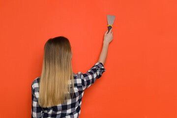 Young Woman Working With Painter's Spatula On Orange Wall. Rear View.