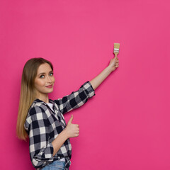 Beautiful Young Woman Is Painting Pink Wall And Showing Thumb Up