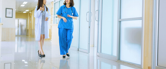 Surgeon and Female Doctor Walk Through Hospital Hallway, They Consult Digital Tablet Computer while Talking about Patient's Health. Modern Bright Hospital with Professional Staff...