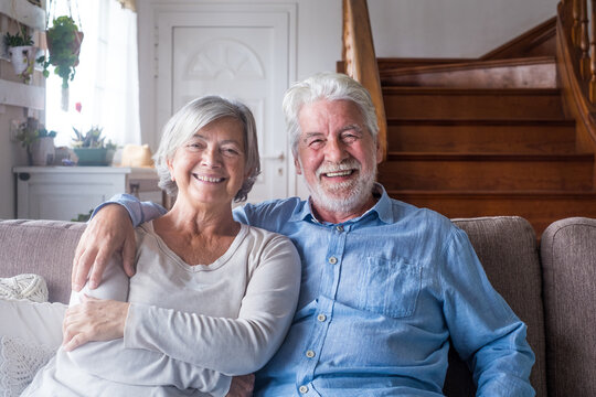 Portrait of happy middle aged retired family couple relaxing on cozy sofa at home. Smiling sincere loving mature senior homeowners looking at camera, posing for photo, showing love and care indoors..