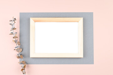 Wooden photo frame with white blank card and flowers on pastel pink background. Mock up poster frame. Stylish template