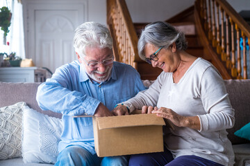 Happy mature aged older family couple unpacking carton box, satisfied with internet store purchase or unexpected gift, feeling excited of fast delivery shipping service, positive shopping experience..