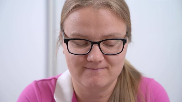 Portrait of young blonde woman with ponytail and glasses who is concentrating on problem, she is nervous and thoughtfully moves her lips, front view.