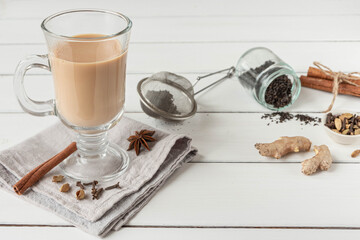 A glass of hot Indian masala tea brewed with aromatic spices and milk. White wooden background, copy space