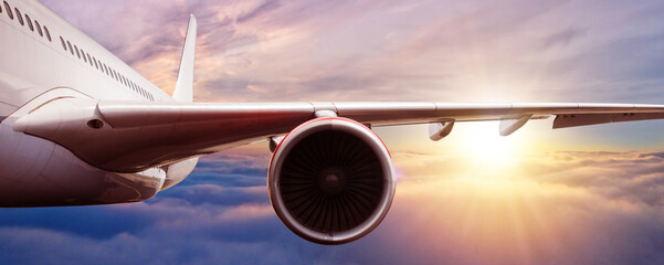 Detail of jetplane wing flying above clouds in sunset - obrazy, fototapety, plakaty