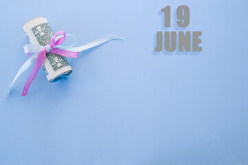 calendar date on blue background with rolled up dollar bills pinned by blue and pink ribbon with copy space. June 19 is the twenty-second day of the month