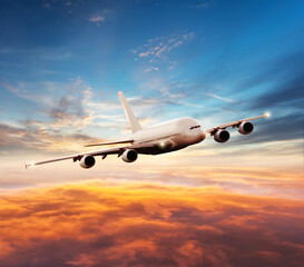 Naklejka na ściany i meble Passenger jetplane flying above clouds in sunset