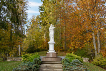 Statue of the Virgin Mary in the park near the lake Vita, Carpathian mountains, Nyzhnii Studenyi, Zakarpattia region, Ukraine. Warm sunny autumn day in a garden. Leaf fall landscape, colors of autumn.
