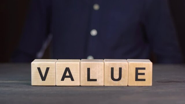 A man in a shirt composes the word VALUE from wooden cubes, close up.