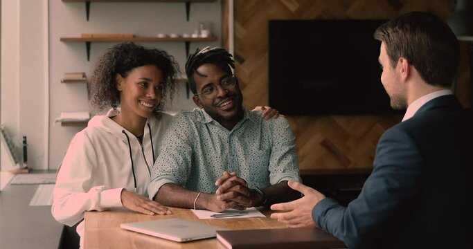 Happy young african american couple meeting male real estate agent in office, signing contract, feeling excited of purchasing new own apartment or house, shaking hands celebrating closing deal.