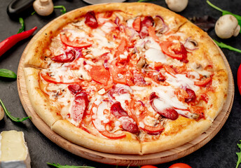 pizza with sausages, mushrooms, tomatoes and cheese on a stone background