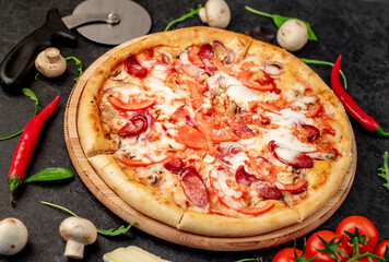 pizza with sausages, mushrooms, tomatoes and cheese on a stone background